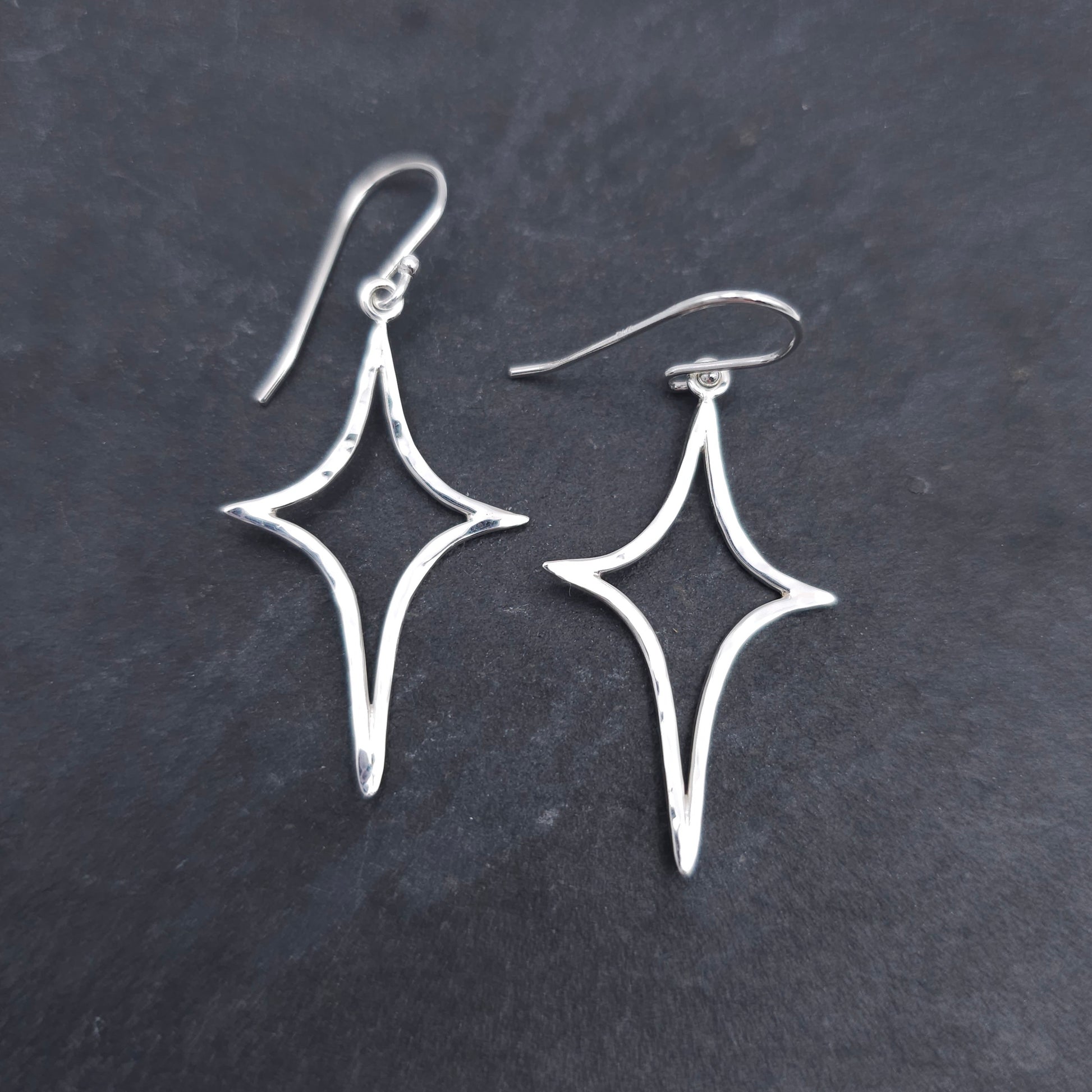 Silver wire formed in an elongated star shape, with a slightly hammered finish, dangling from French earring wires.