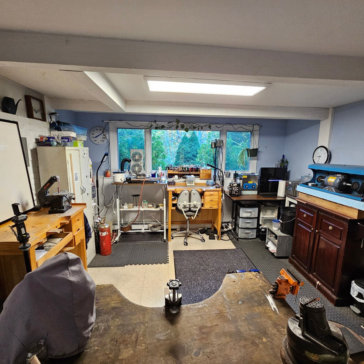 Autumn Designs jewelry studio in York, Maine, with jeweler’s benches, hand tools, a polishing station and a window looking out on evergreen trees