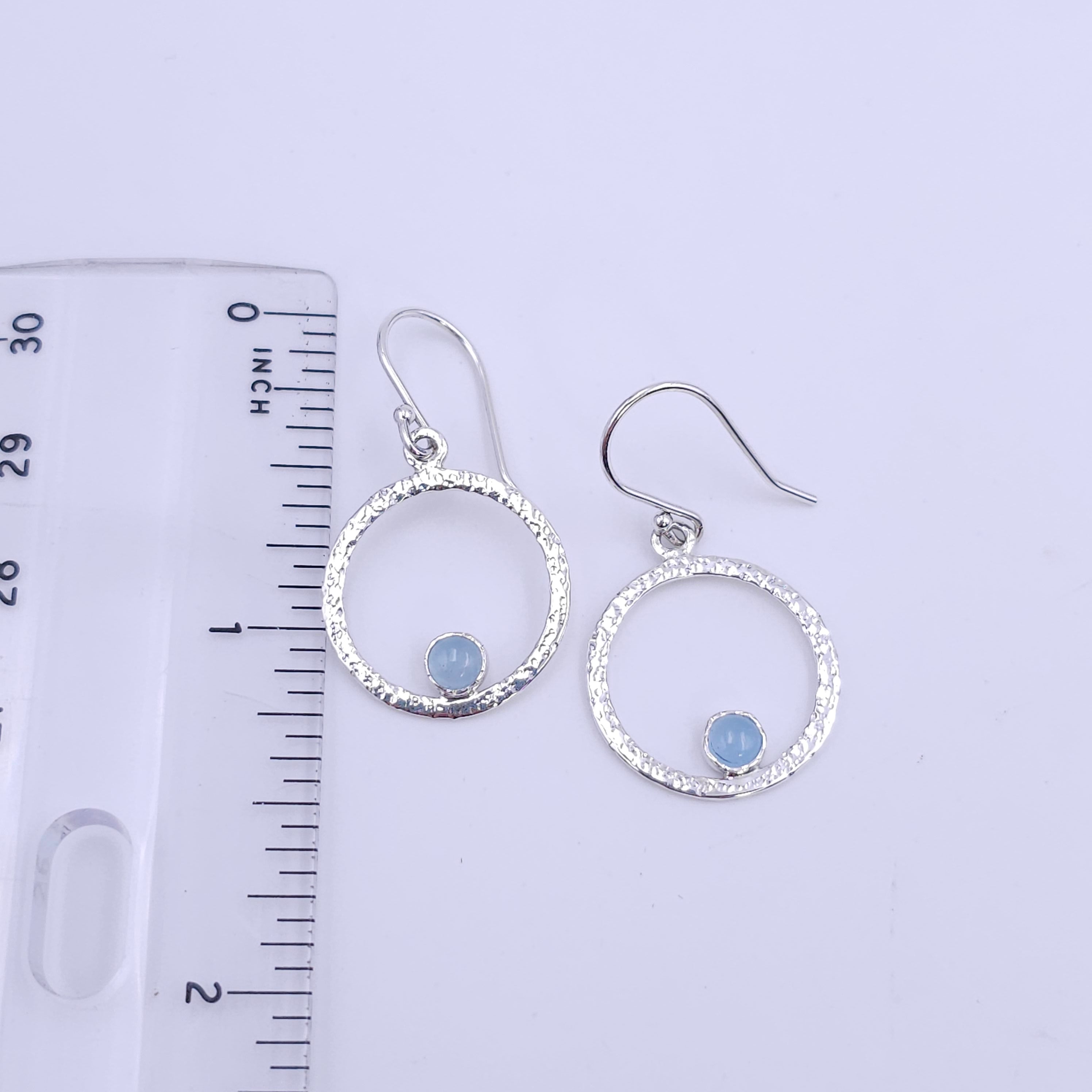 Silver textured circle earrings with blue round aquamarine round stones bezel set on bottom of circle shown with ruler showing 1.25" length