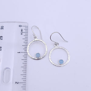 Silver textured circle earrings with blue round aquamarine round stones bezel set on bottom of circle shown with ruler showing 1.25" length