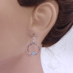 Silver textured circle earrings with blue round aquamarine round stones bezel set on bottom of circle shown on mannequin