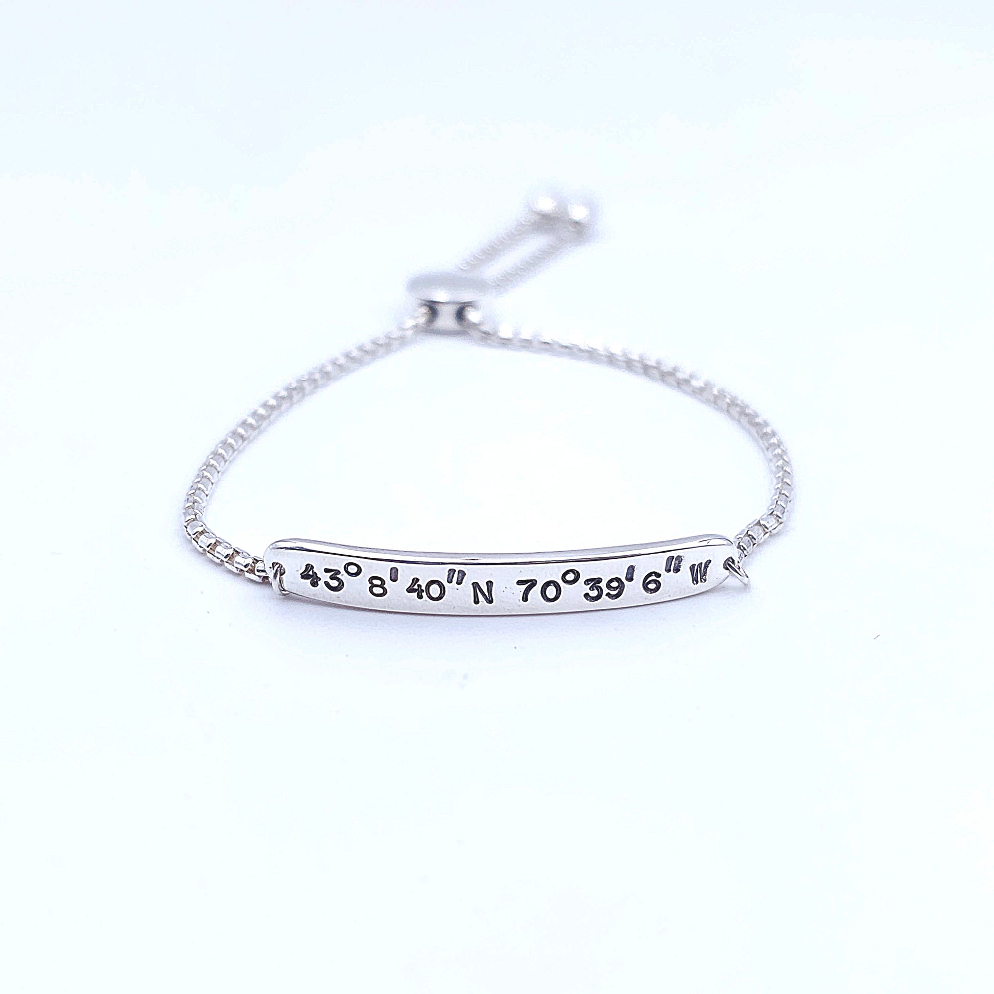 Silver bar with coordinates stamped on it, attached to adjustable silver slider chain.