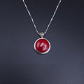 A silver necklace with a round orangish-red cabochon pendant and a fancy swirly oxidized bail. On a silver station chain with a silver bead every 1/2"