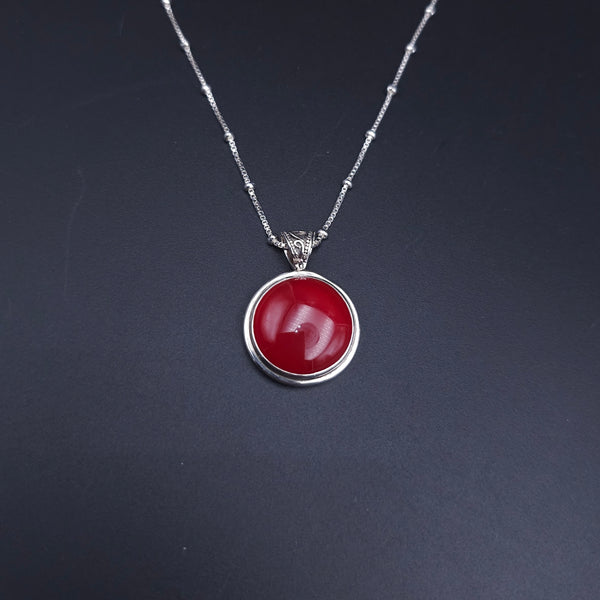 A silver necklace with a round orangish-red cabochon pendant and a fancy swirly oxidized bail. On a silver station chain with a silver bead every 1/2"