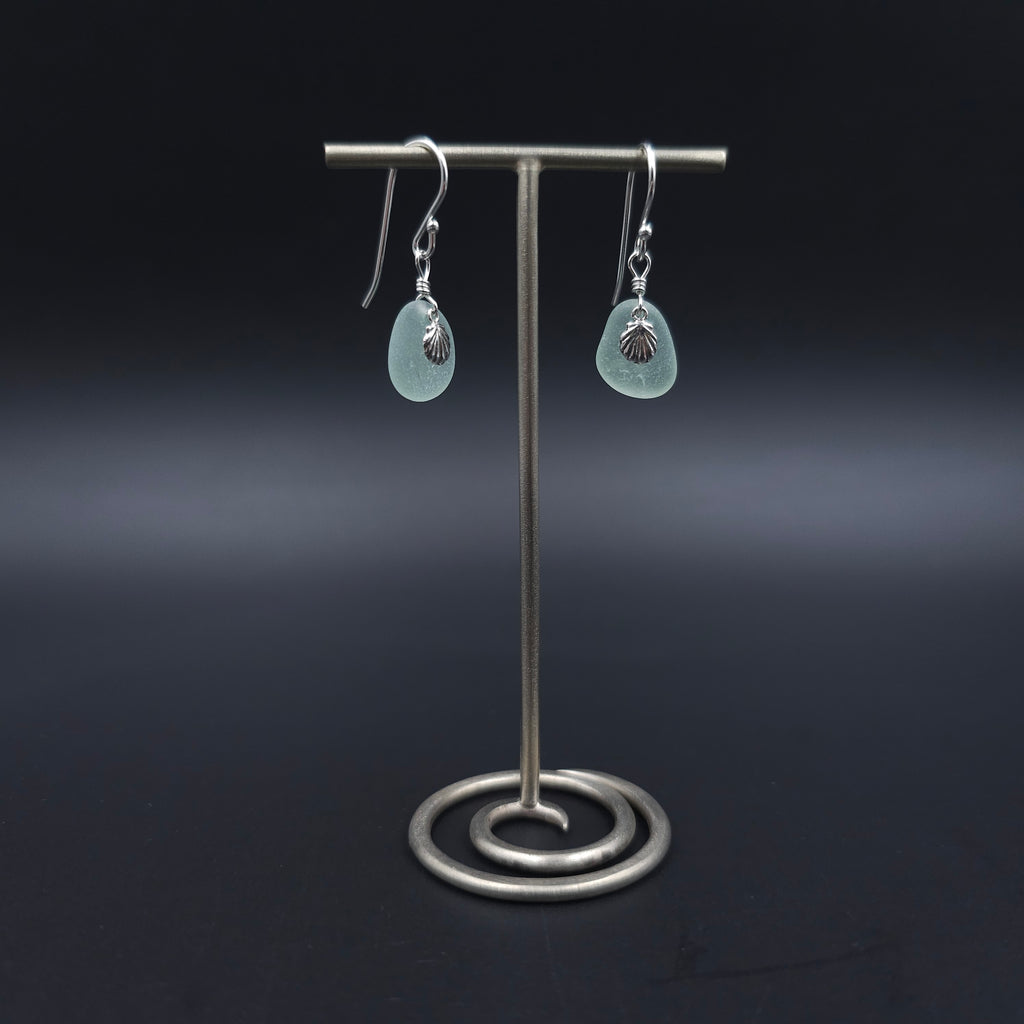 Silver dangle earrings with teardrop shaped sea foam sea glass with tiny shell charms sitting on top of sea glass