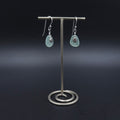 Silver dangle earrings with teardrop shaped sea foam sea glass with tiny shell charms sitting on top of sea glass