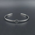 A polished silver cuff bracelet with a small circular charm featuring an engraved outline of the state of Maine attached to the center of the cuff.