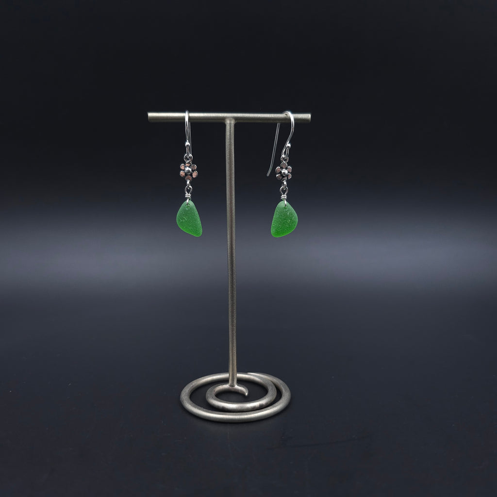 Green sea glass dangle earrings with tiny flower charms dangling between earring wires and green sea glass