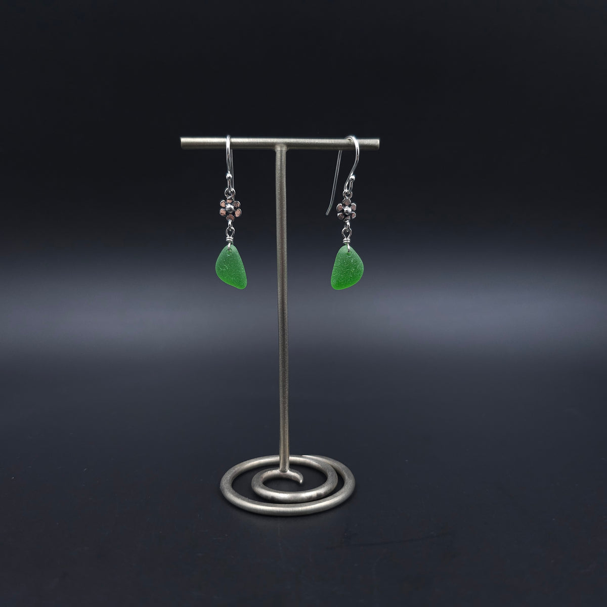 Green sea glass dangle earrings with tiny flower charms dangling between earring wires and green sea glass