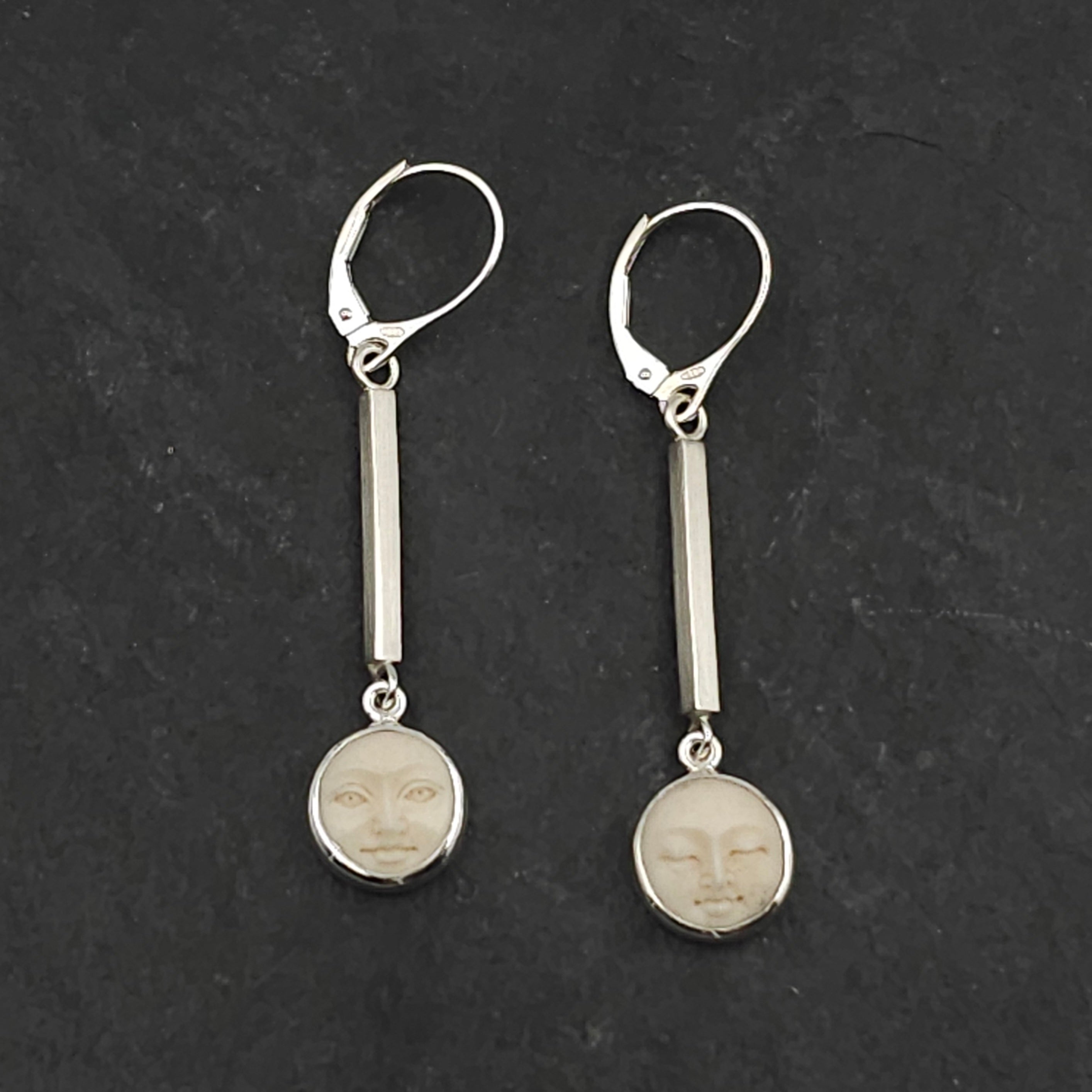 Pair of silver earrings with bezel set carved face designs hanging from square brushed finished silver pieces
