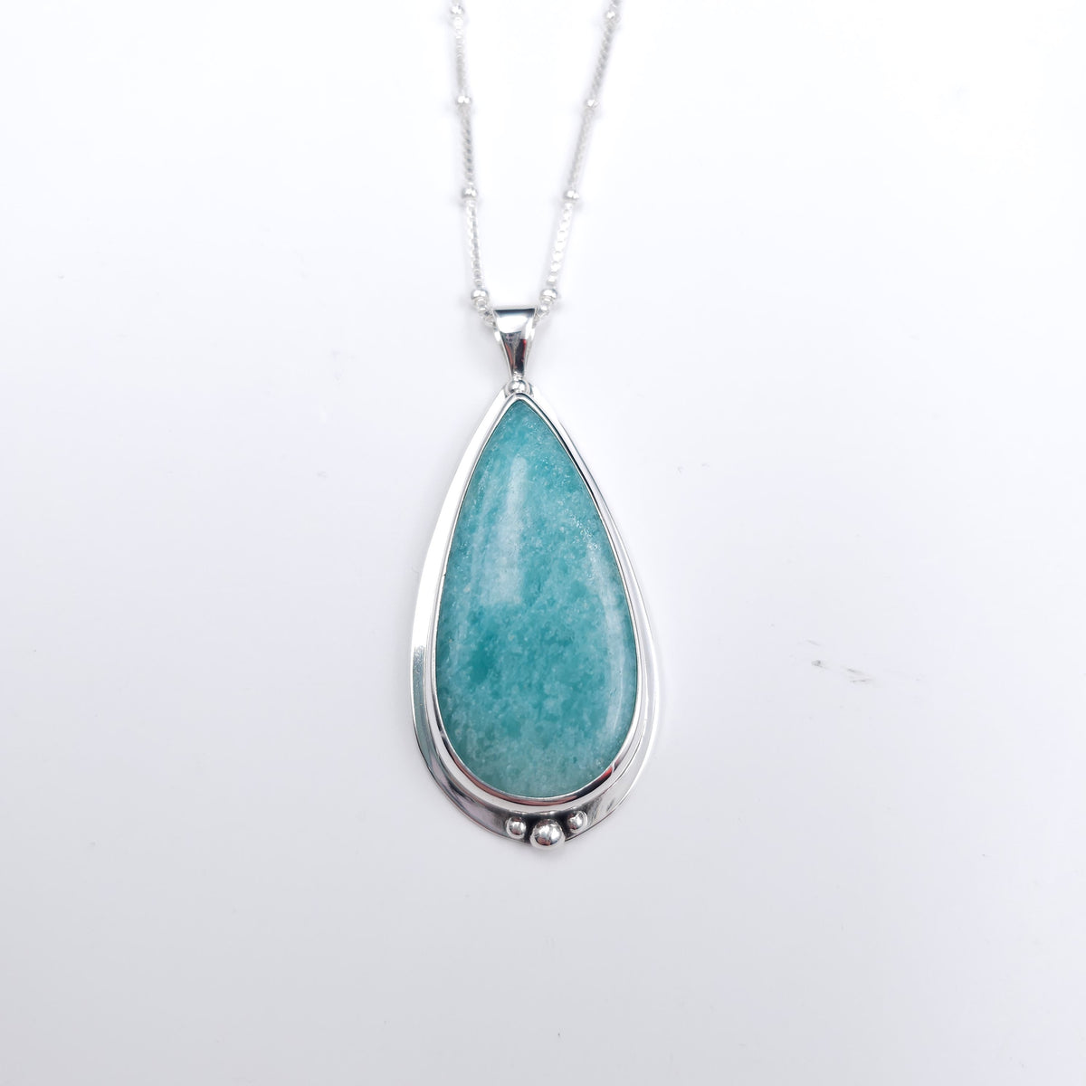 A teardrop-shaped pendant necklace featuring a polished turquoise-blue amazonite stone in a silver bezel setting