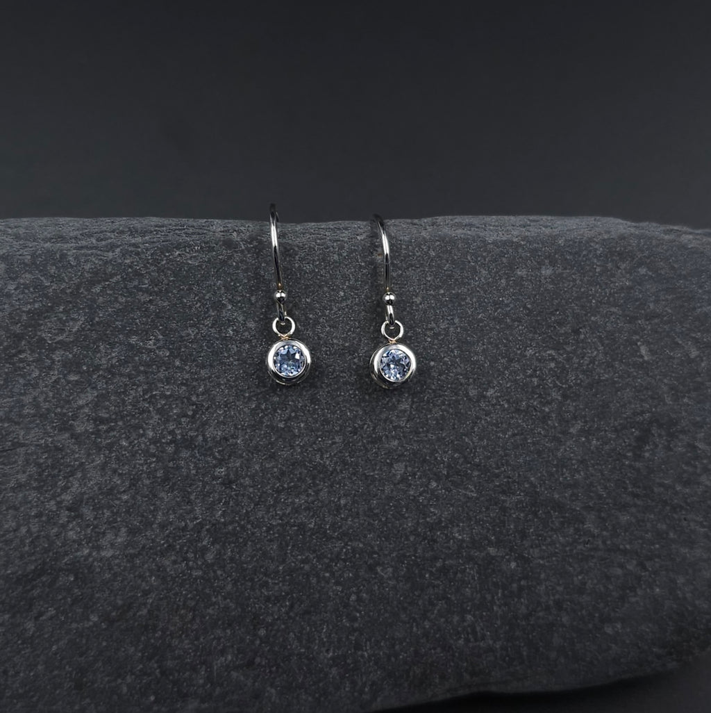Faceted round light blue stone set in silver bezel and hanging from French earring wires.