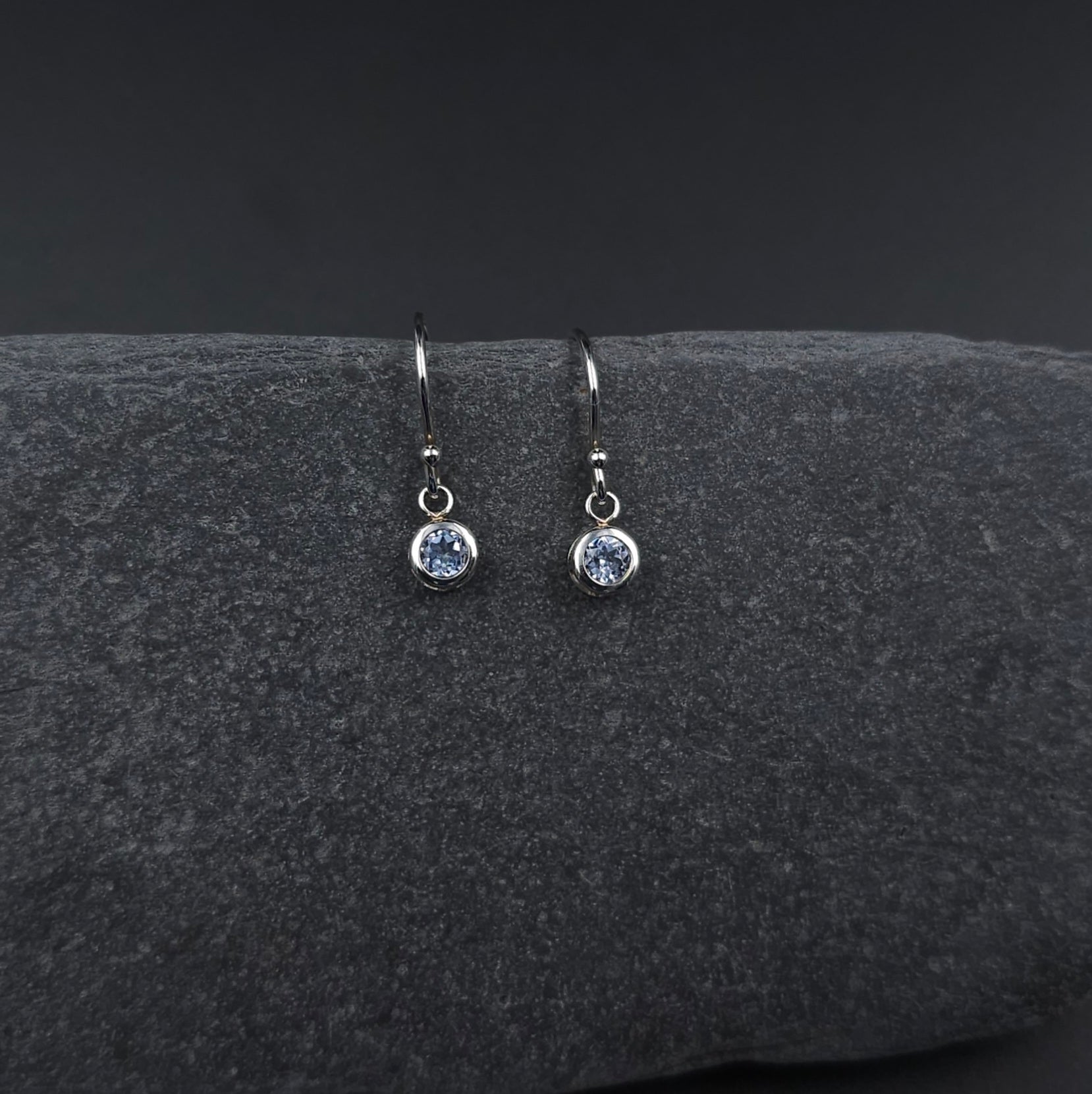 Faceted round light blue stone set in silver bezel and hanging from French earring wires.