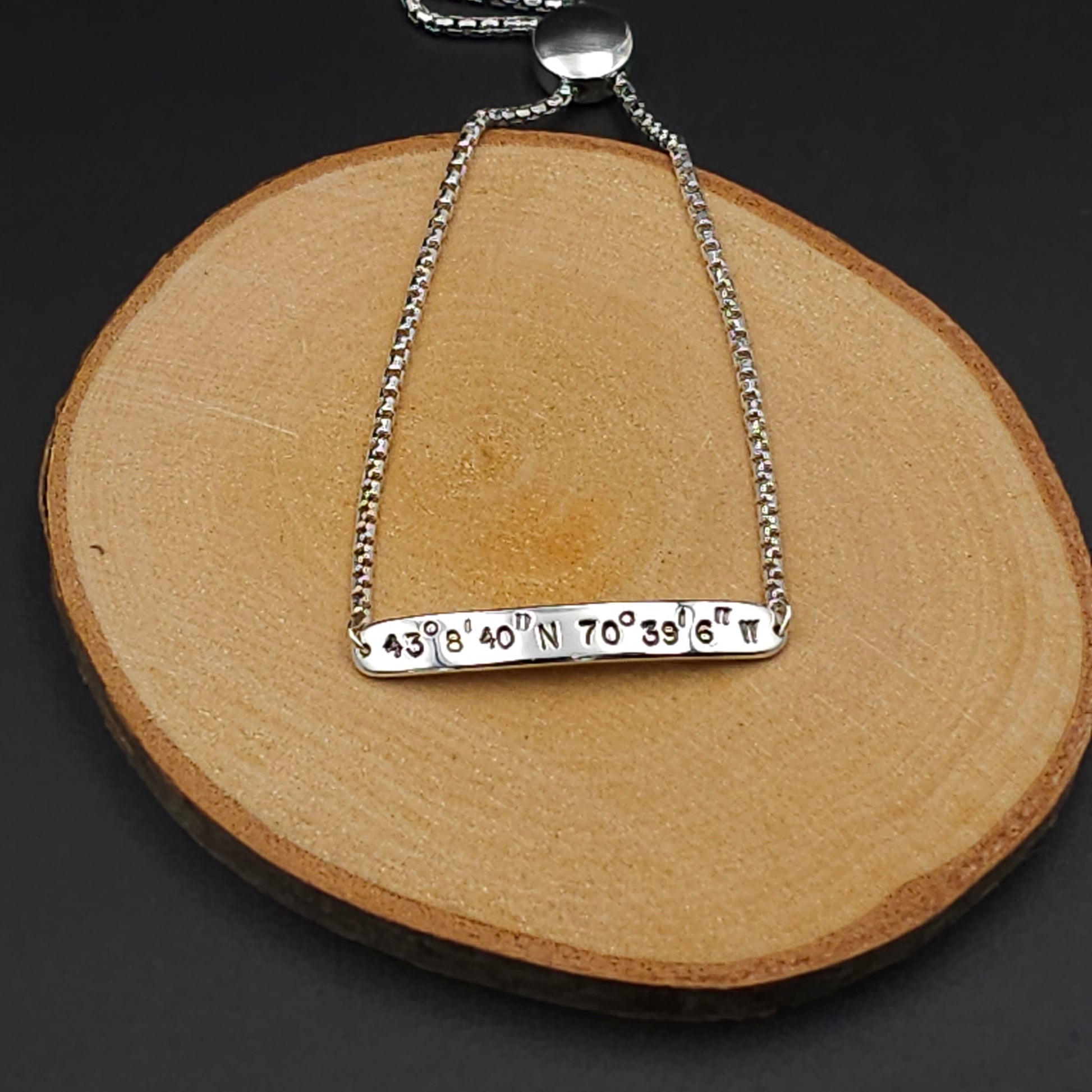 Silver bar with coordinates stamped on it, attached to an adjustable silver slider chain.