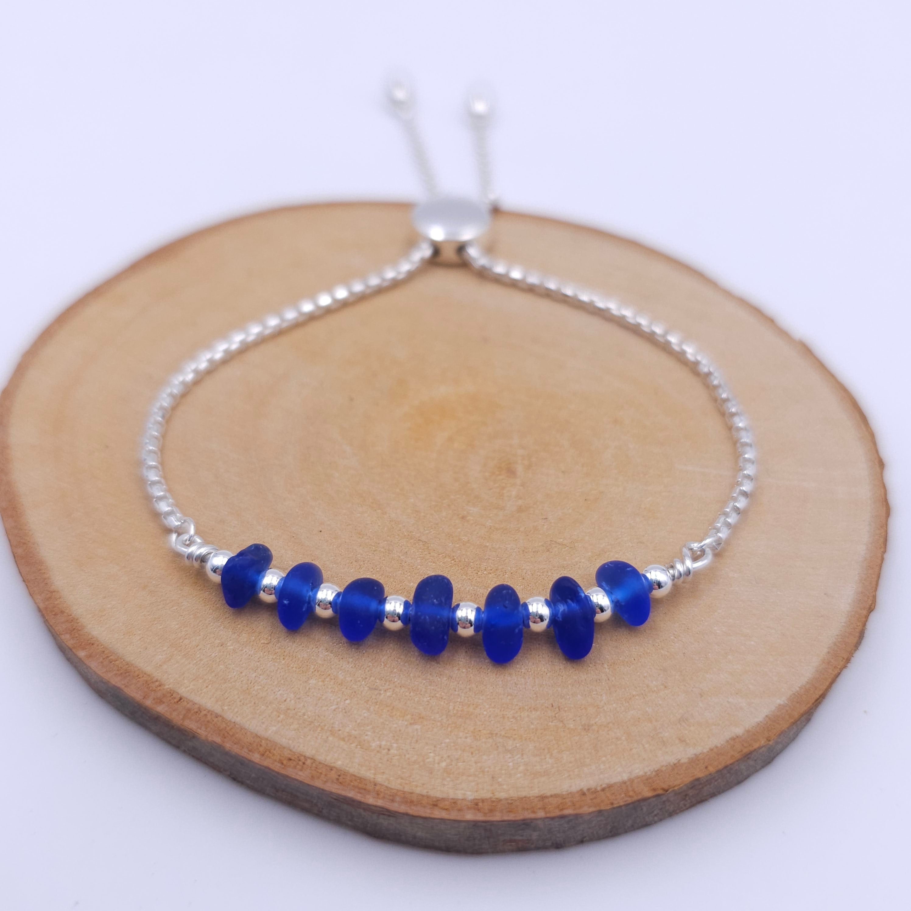 Silver adjustable slider chain bracelet with 7 pieces of cobalt blue drilled sea glass on top, separated by small silver round beads.