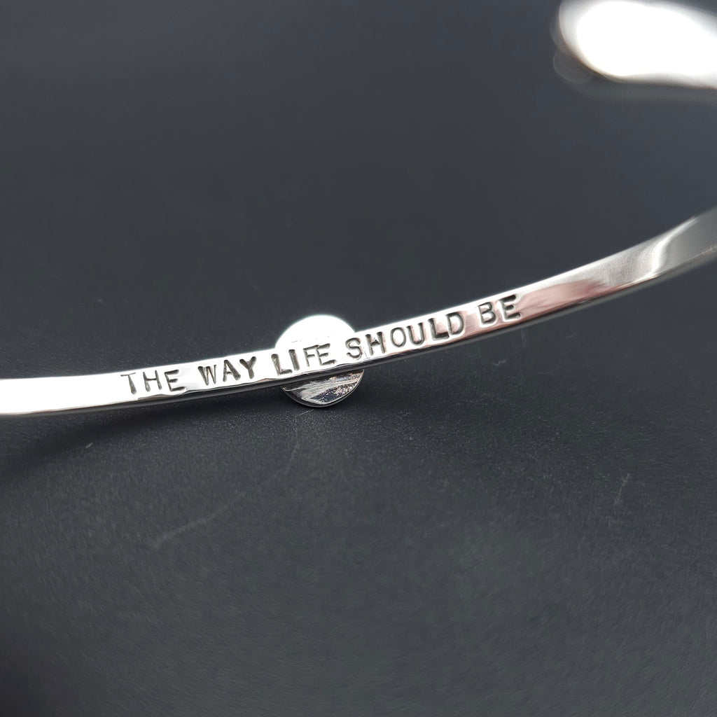 The inside of a silver metal bangle bracelet with the engraved text 'THE WAY LIFE SHOULD BE' 