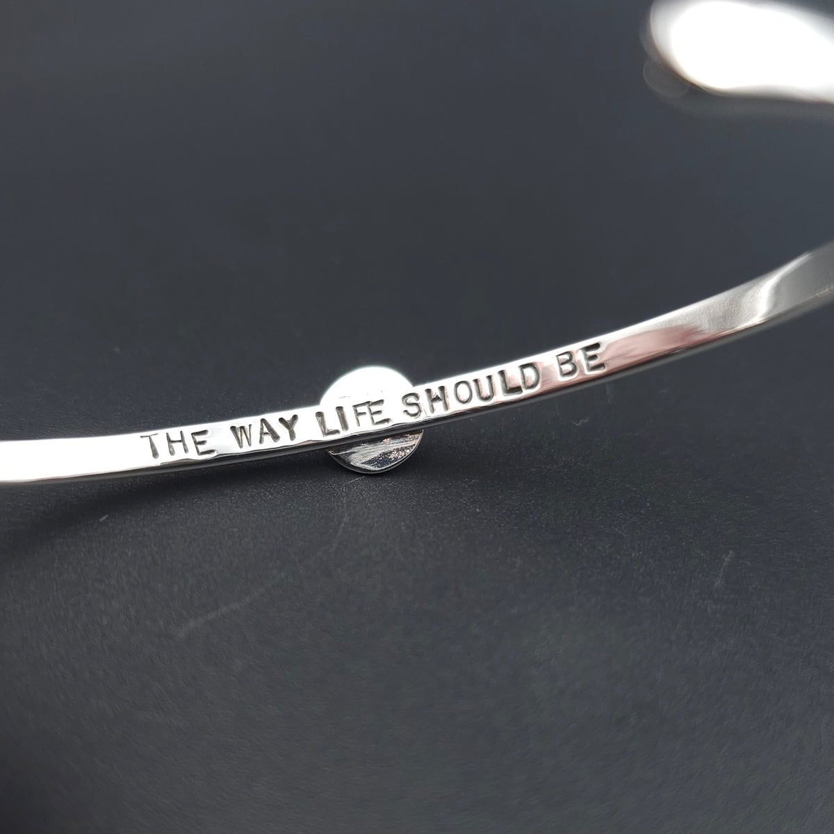 The inside of a silver metal bangle bracelet with the engraved text 'THE WAY LIFE SHOULD BE' 