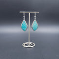A pair of silver drop earrings with pointed teardrop-shaped turquoise-blue stone.