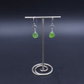 A pair of silver dangle earrings with small green teardrop-shaped sea glass, hanging from small silver circles.