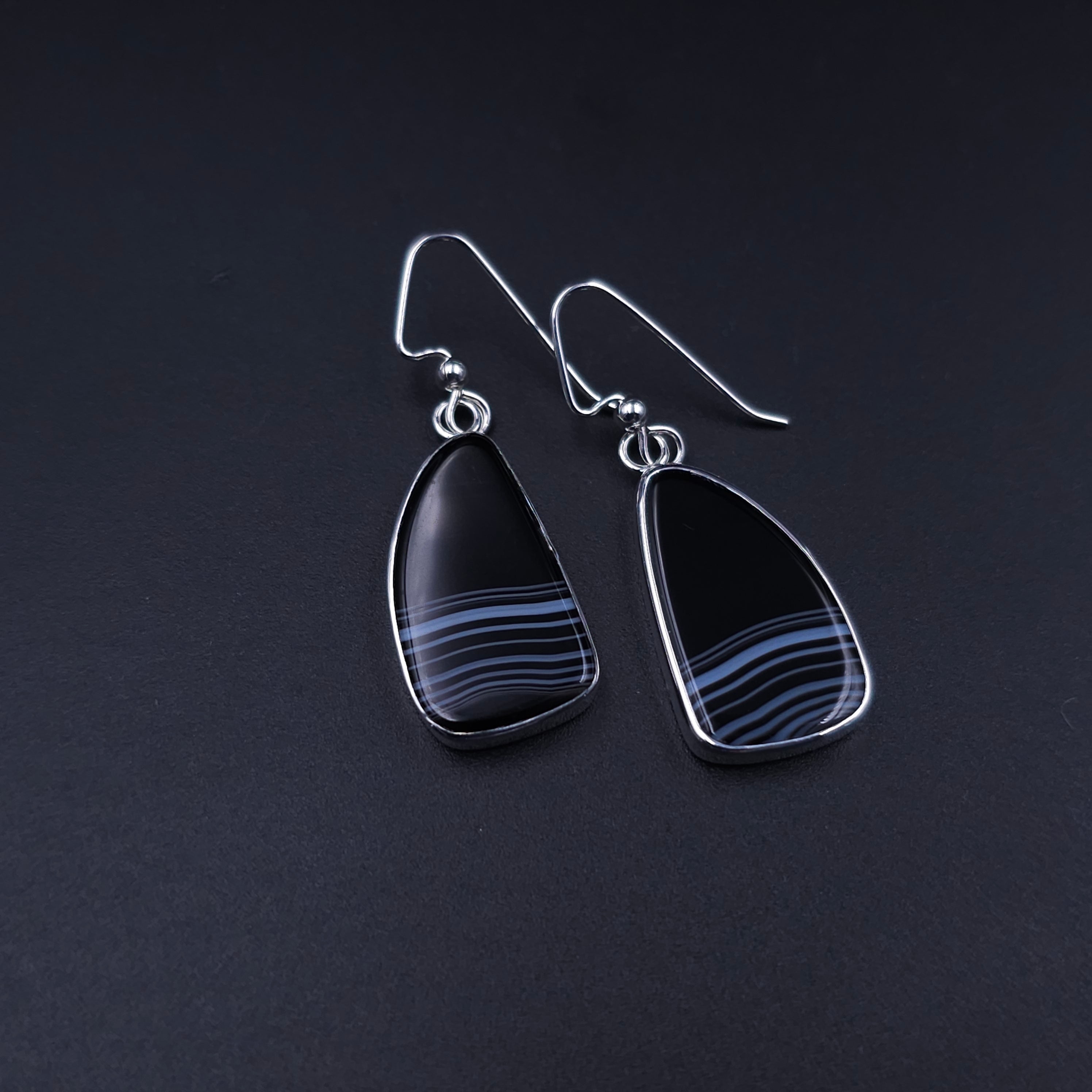 freeform teardrop shaped black onyx stones with white stripes at the bottom bezel set in silver with french earring wires