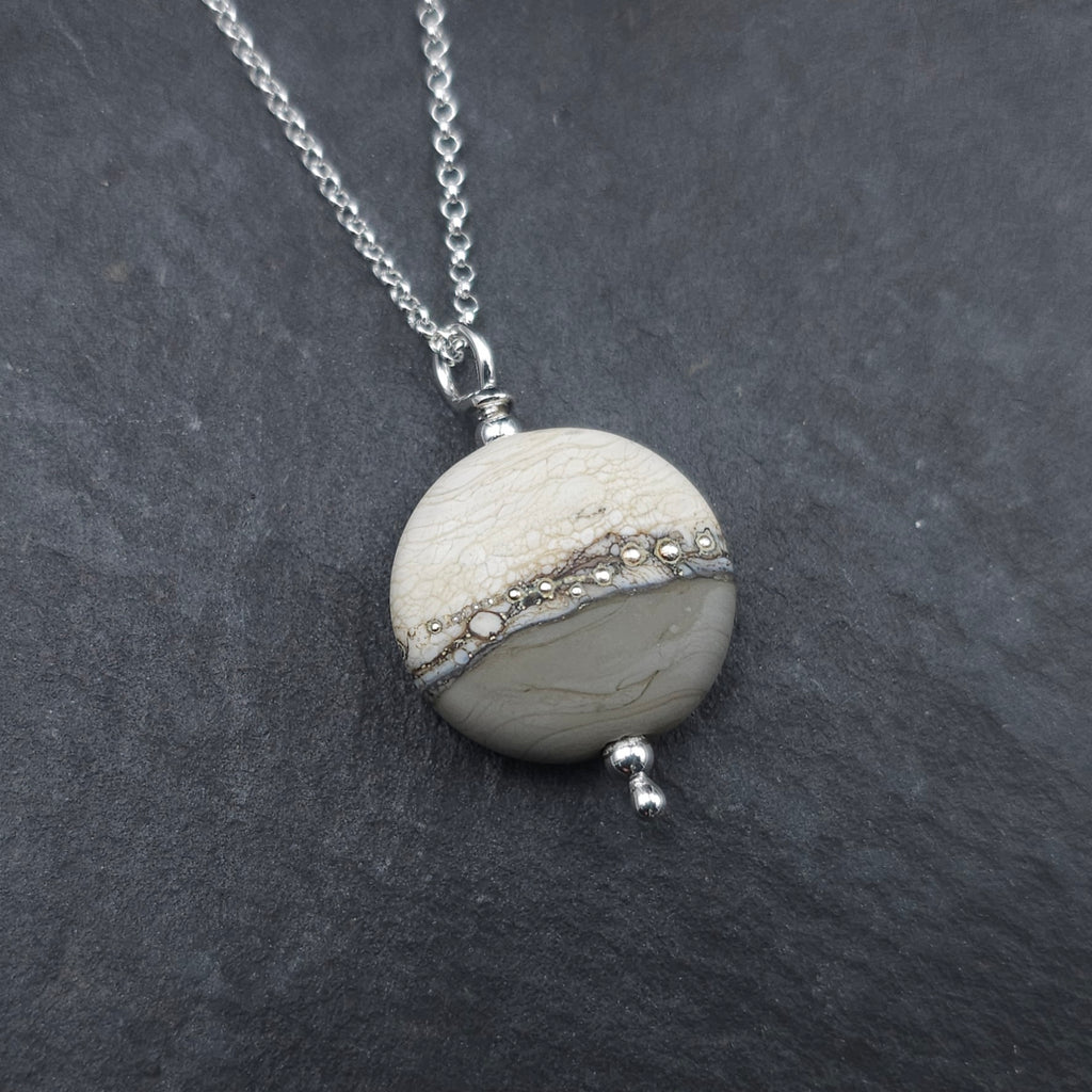 Round bead pendant with beige on top and gray on bottom with silver beads across the center