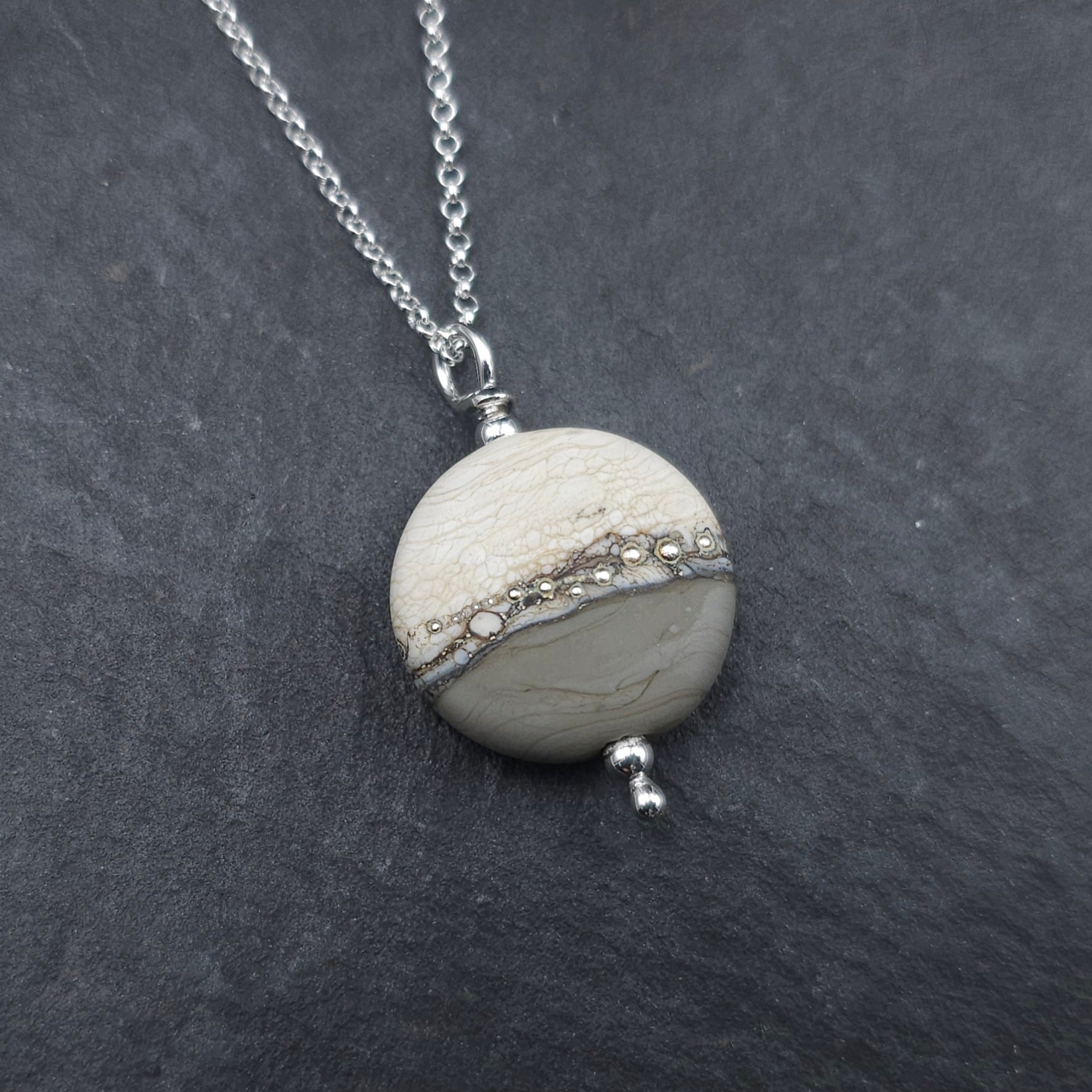Round bead pendant with beige on top and gray on bottom with silver beads across the center