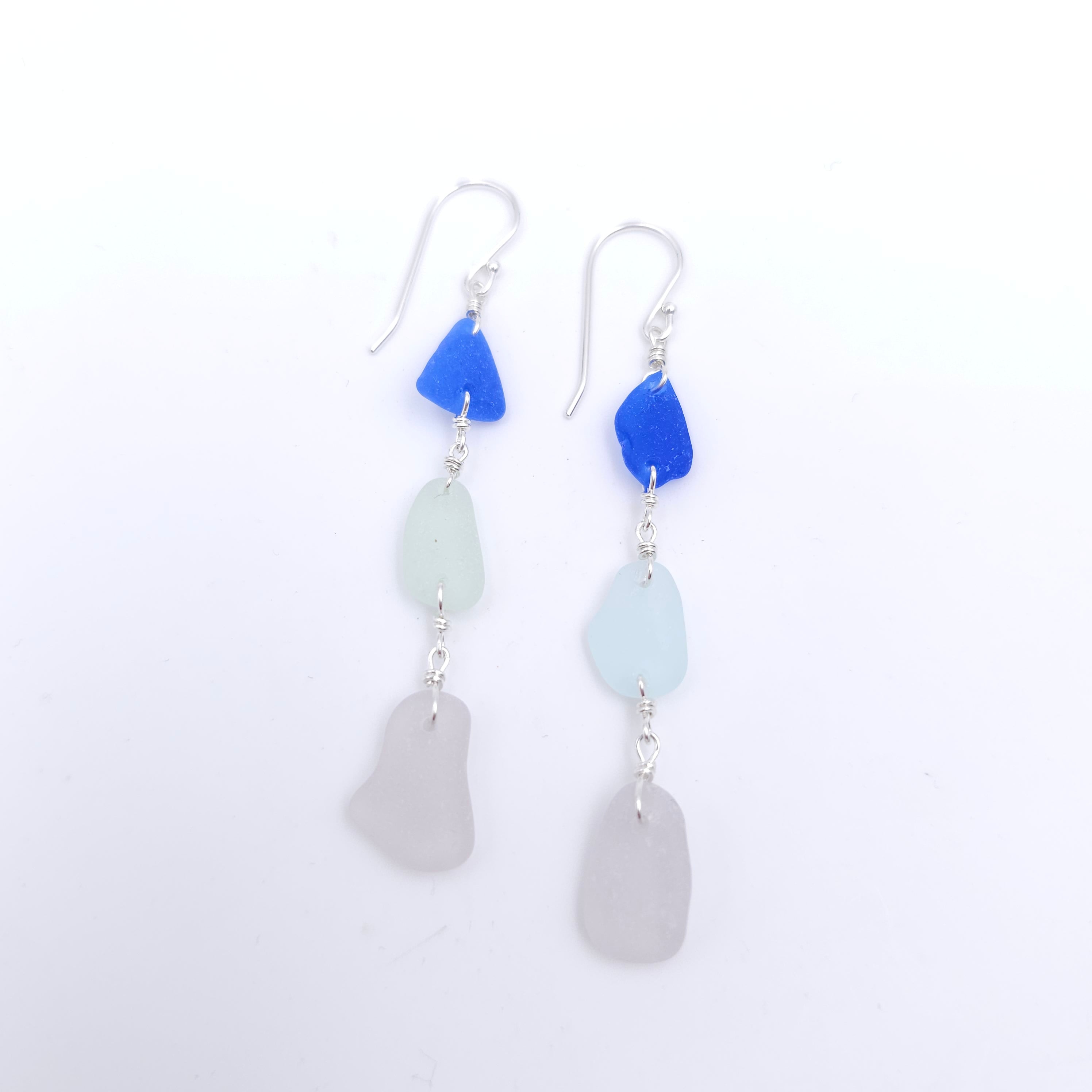 Three pieces of sea glass: dark blue, light blue, and light purple, dangle earrings.