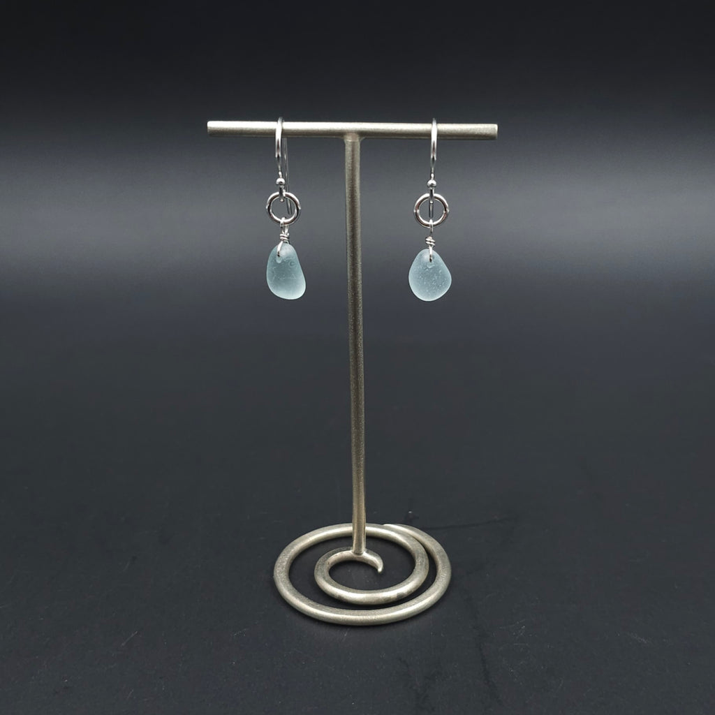 A pair of silver drop earrings with light blue teardrop-shaped sea glass hanging from silver circles and then from French earring wires