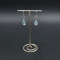 A pair of silver drop earrings with light blue teardrop-shaped sea glass hanging from silver circles and then from French earring wires