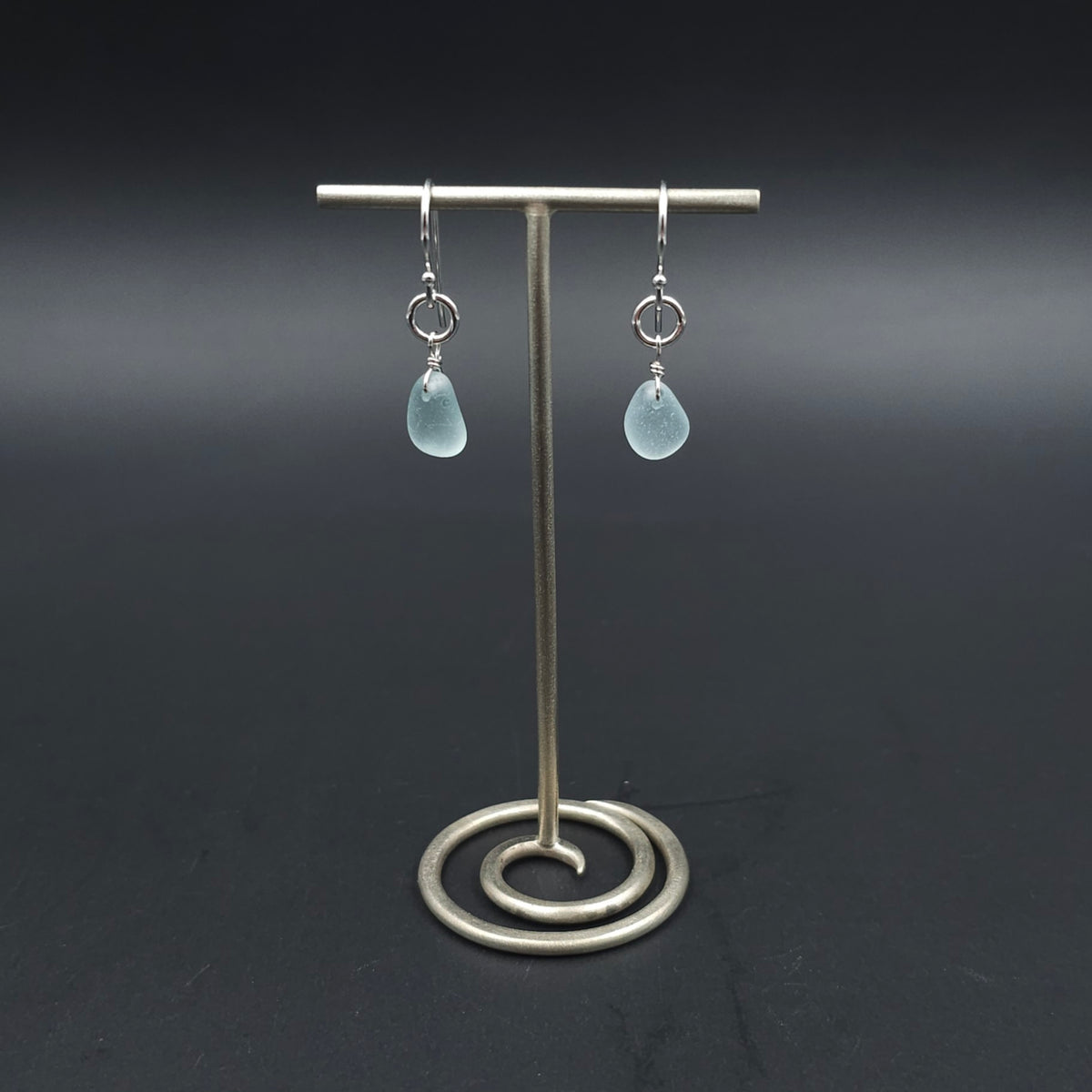 A pair of silver drop earrings with light blue teardrop-shaped sea glass hanging from silver circles and then from French earring wires