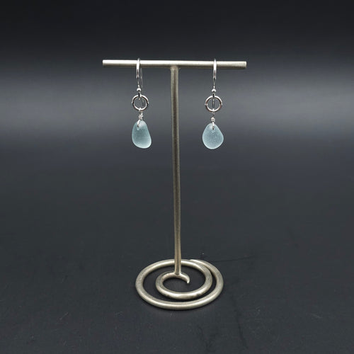 A pair of silver drop earrings with light blue teardrop-shaped sea glass hanging from silver circles and then from French earring wires