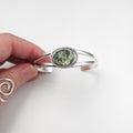 Sterling cuff made from two pieces of half round wire connected in the back and open on the top. Bezel set stone with dark green and clear natural patterns. A textured silver border surrounds the stone.
