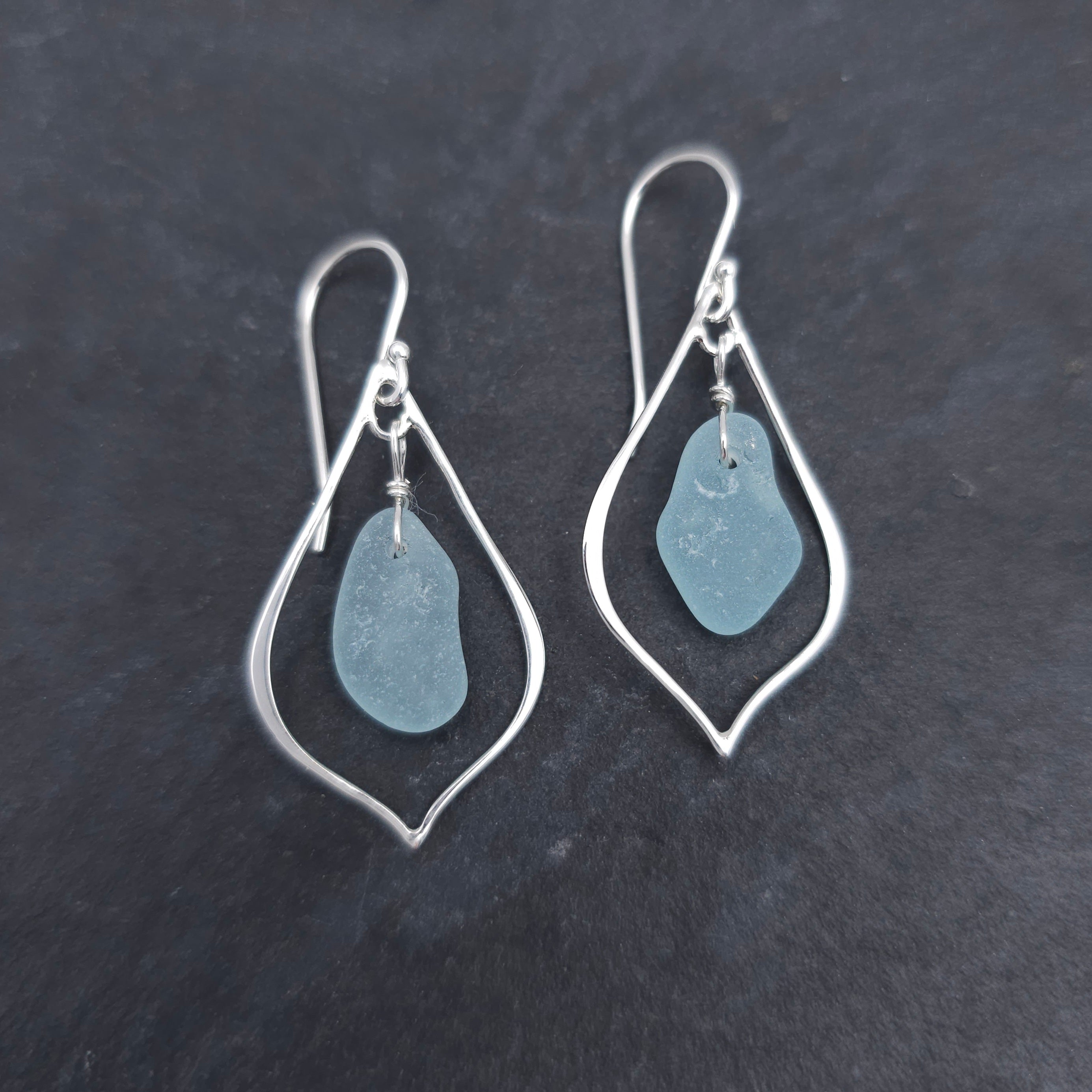 Silver wire in the shape of a pointed teardrop with light blue sea glass dangling inside the earrings.