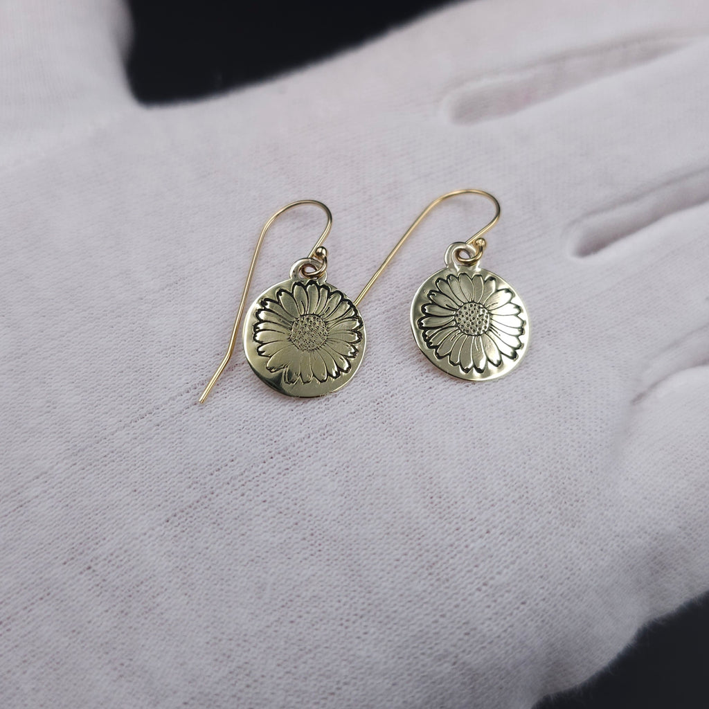 Round disc brass earrings with a daisy stamped in center of disc, hanging from french earrings wires
