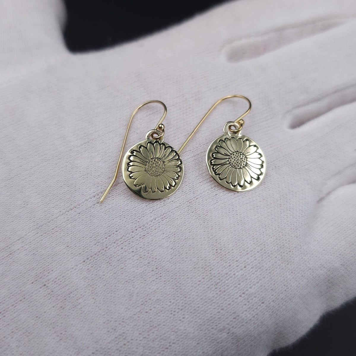 Round disc brass earrings with a daisy stamped in center of disc, hanging from french earrings wires