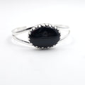 Silver bracelet with a black stone set in a fancy crown bezel setting. Cuff bracelet is made from two half round wire pieces attached at the ends but open in the center.
