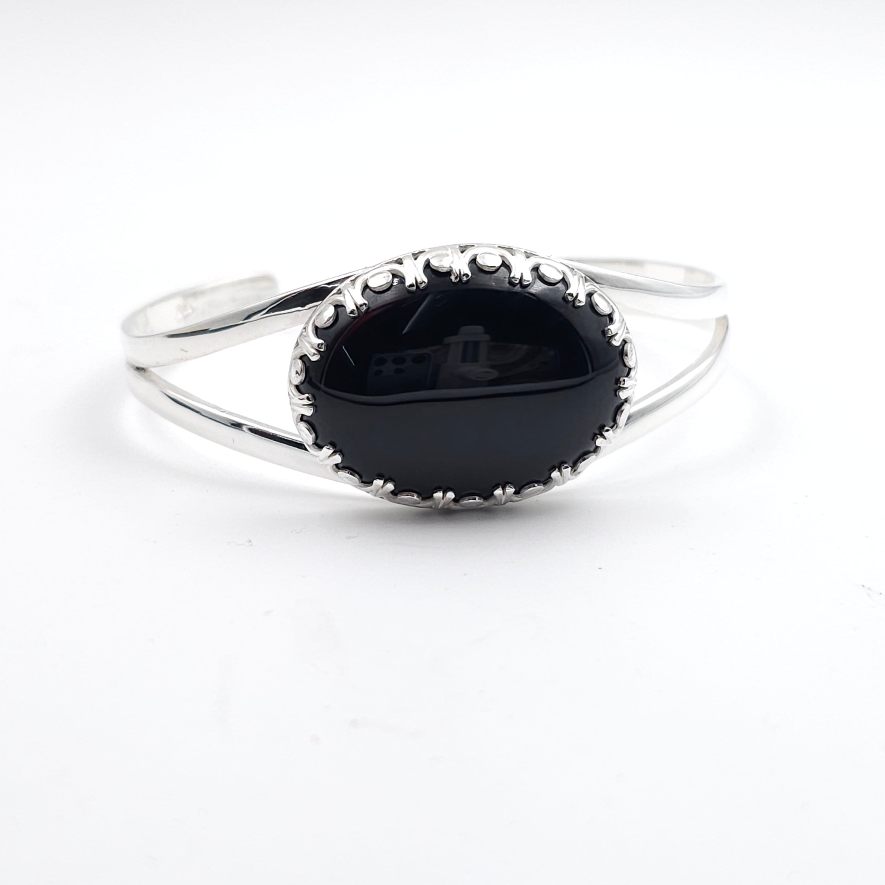 Silver bracelet with a black stone set in a fancy crown bezel setting. Cuff bracelet is made from two half round wire pieces attached at the ends but open in the center.