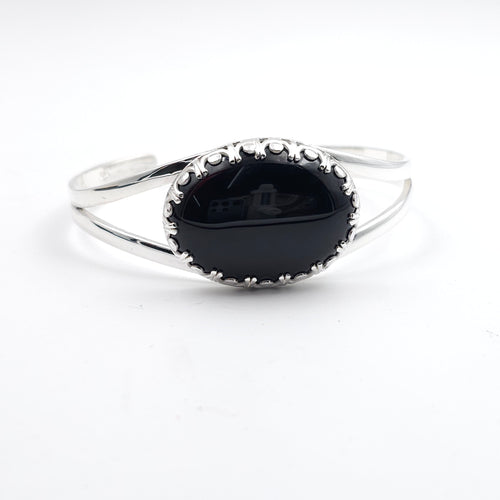 Silver bracelet with a black stone set in a fancy crown bezel setting. Cuff bracelet is made from two half round wire pieces attached at the ends but open in the center.