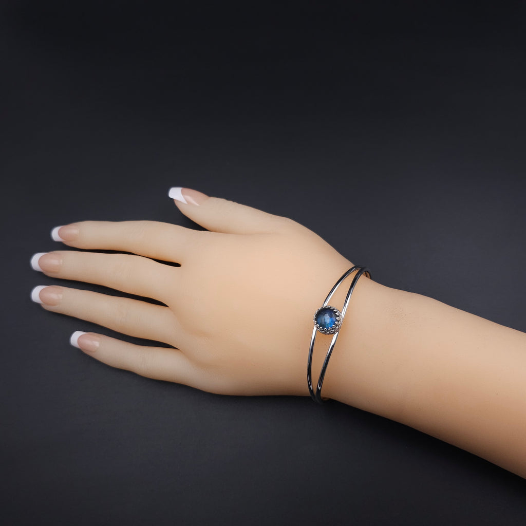 Silver open cuff bracelet with two silver wires open in the middle, with a bezel set round blue labradorite in center