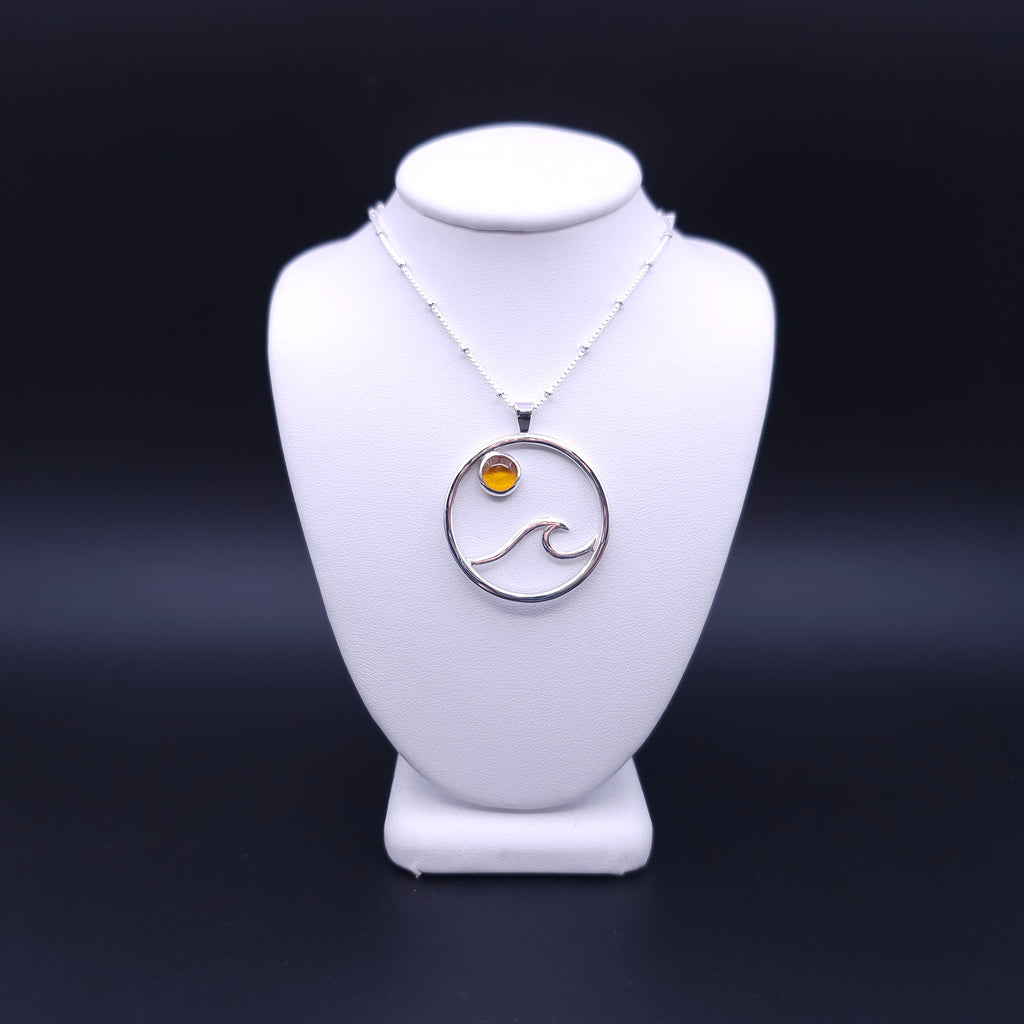 Silver circle pendant with wave made from wire and a round orange amber stone at top of circle slightly off center