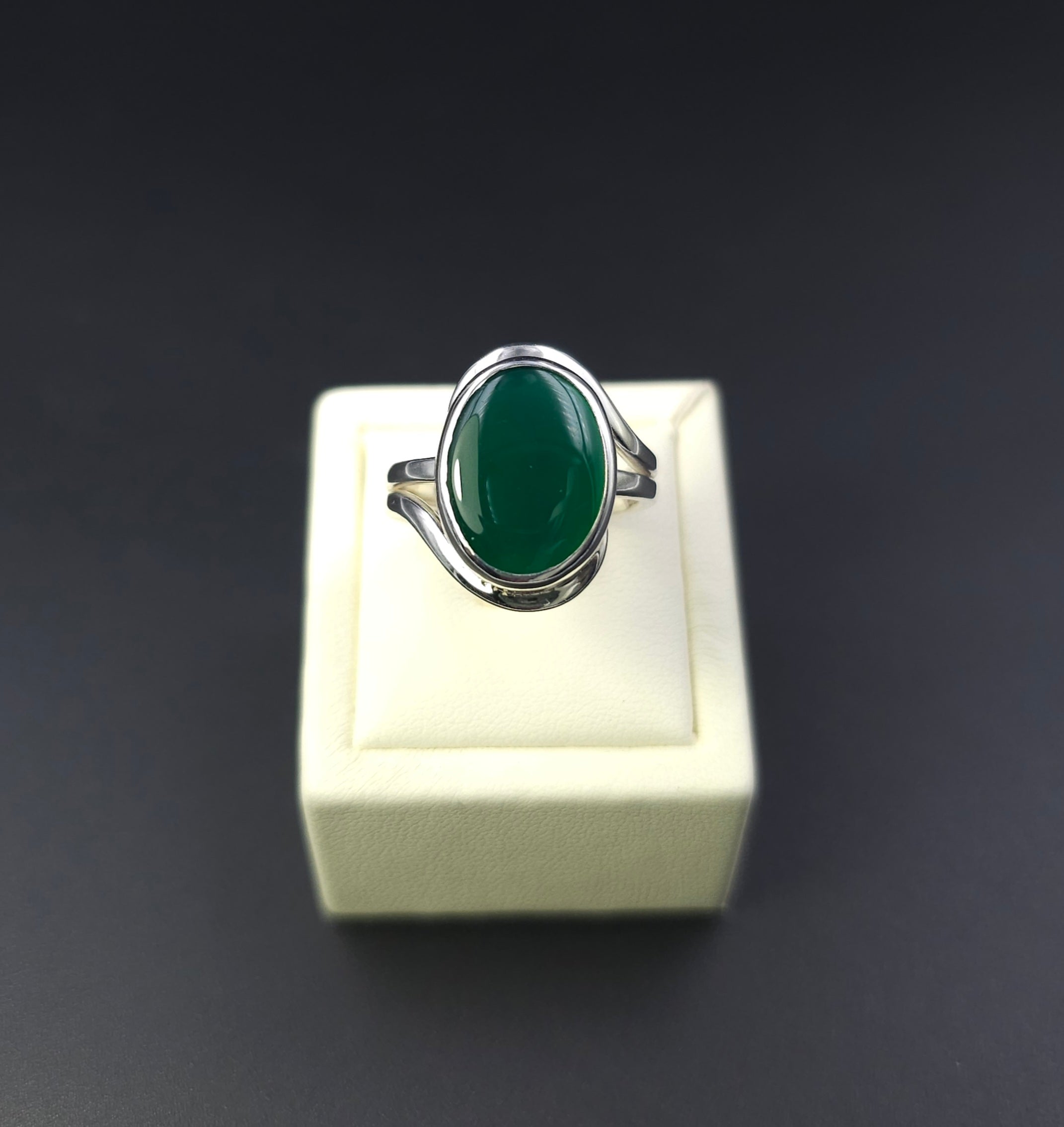 Green oval stone bezel set in silver with silver wire wrapping around the stone on top and bottom, creating a wavy look to the ring.