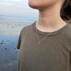 Model at beach wearing necklace with state of Maine outline