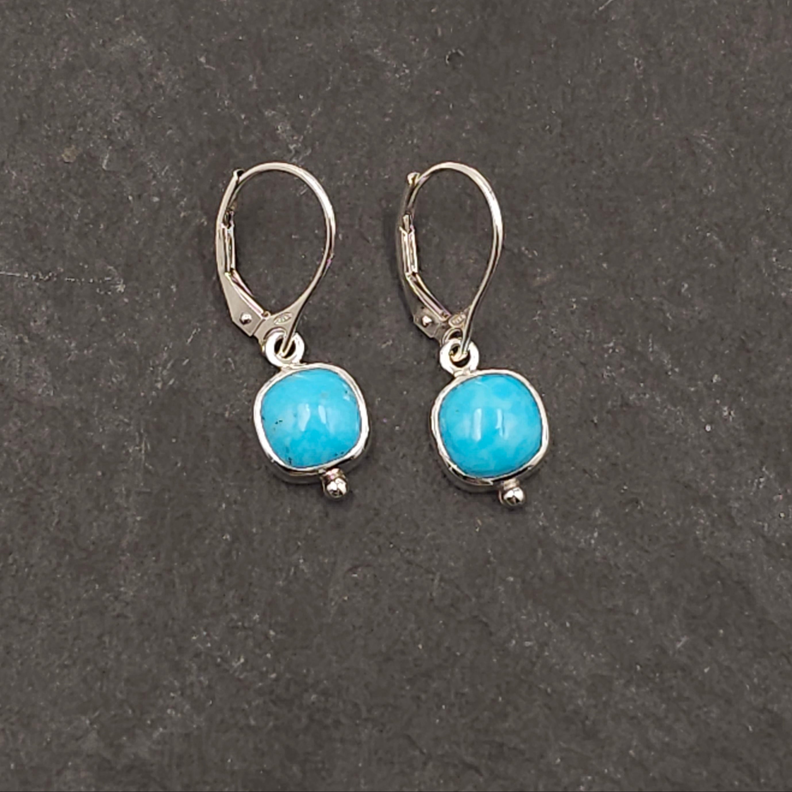 Rounded square turquoise bezel set earrings with small silver ball accent on bottom of bezel, hanging from lever back earring wires.