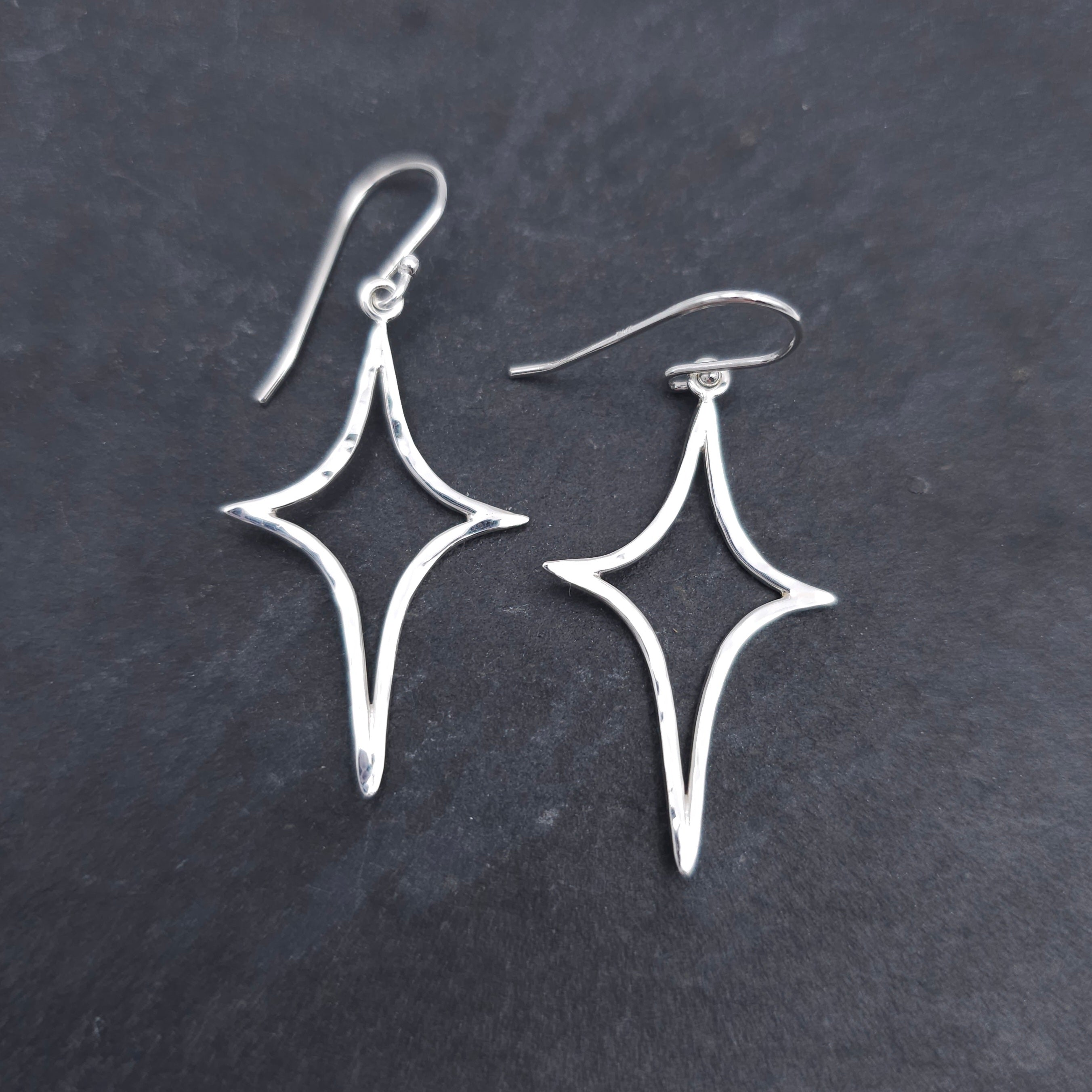 Silver wire formed in an elongated star shape, with a slightly hammered finish, dangling from French earring wires.