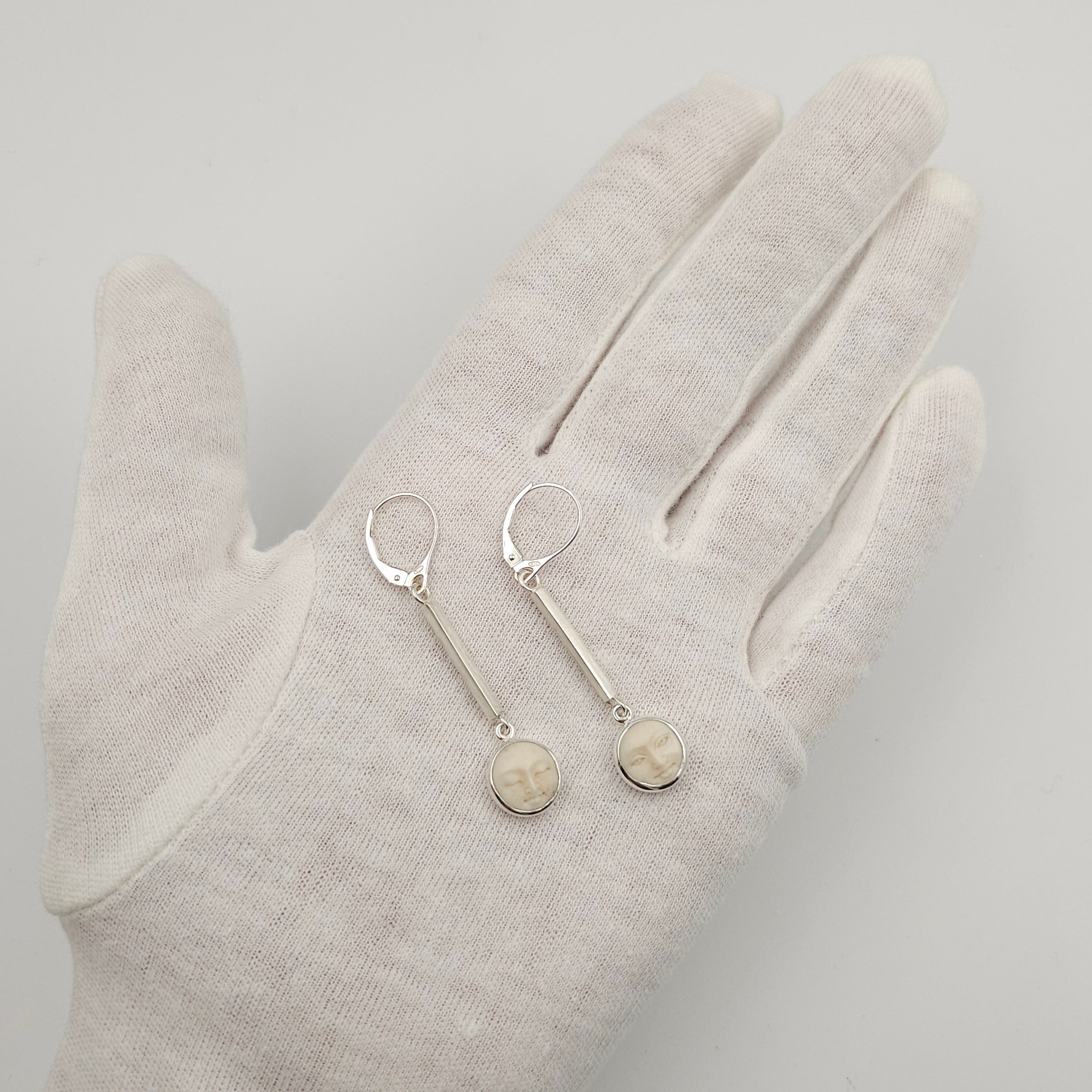 Silver earrings with circular charms on a white glove against a light gray background