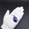 An oval silver pendant necklace with a blue lapis lazuli stone and an oxidized fancy bail, on a snake chain
