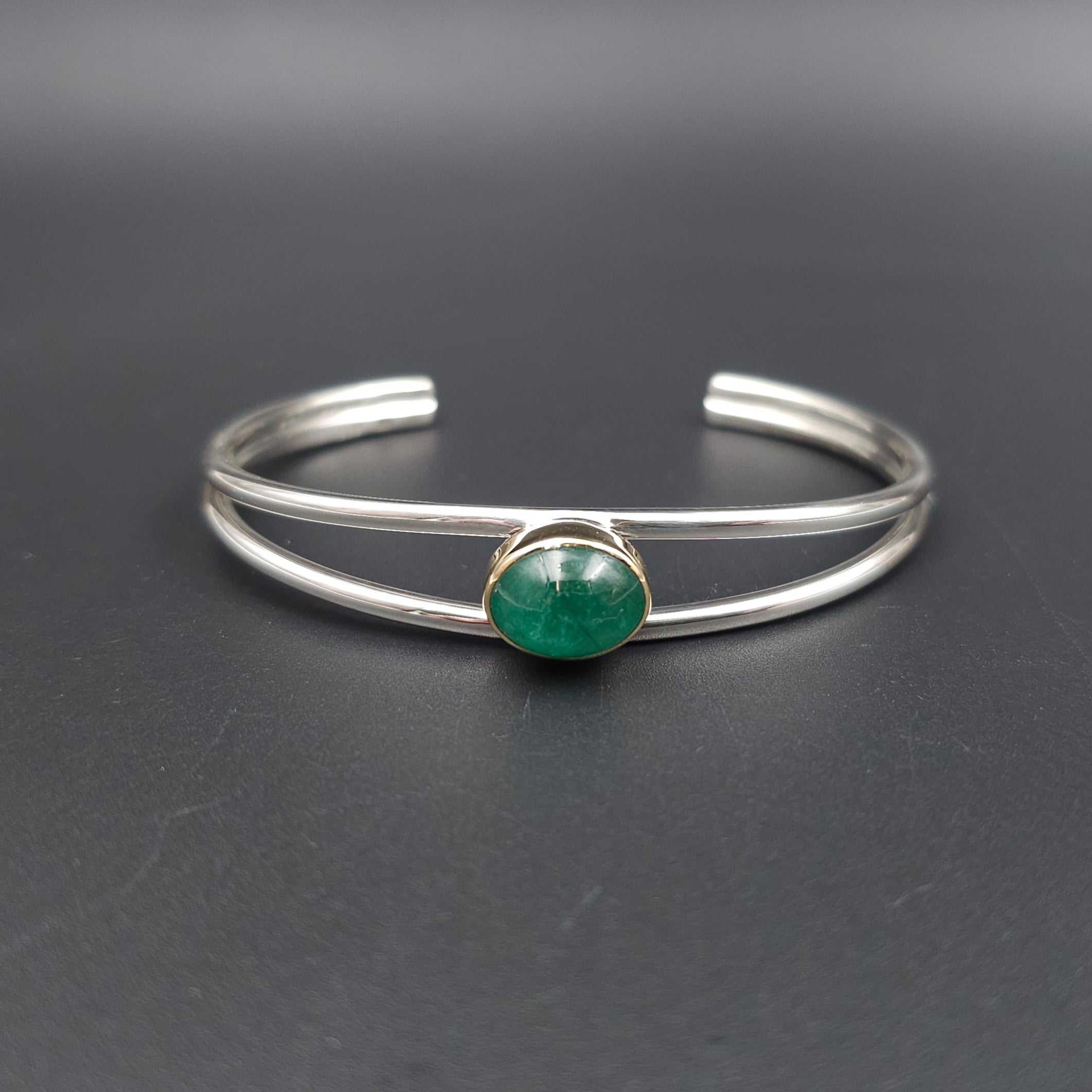 Double wire open cuff silver bracelet with gold bezel set emerald oval cabachon.