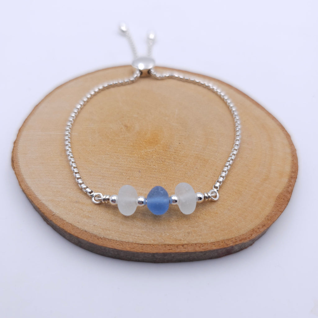Silver chain bracelet with two pieces of white sea glass and one piece of light blue in the center, separated by small silver round beads. A silver bead at the bottom slides to adjust the size.
