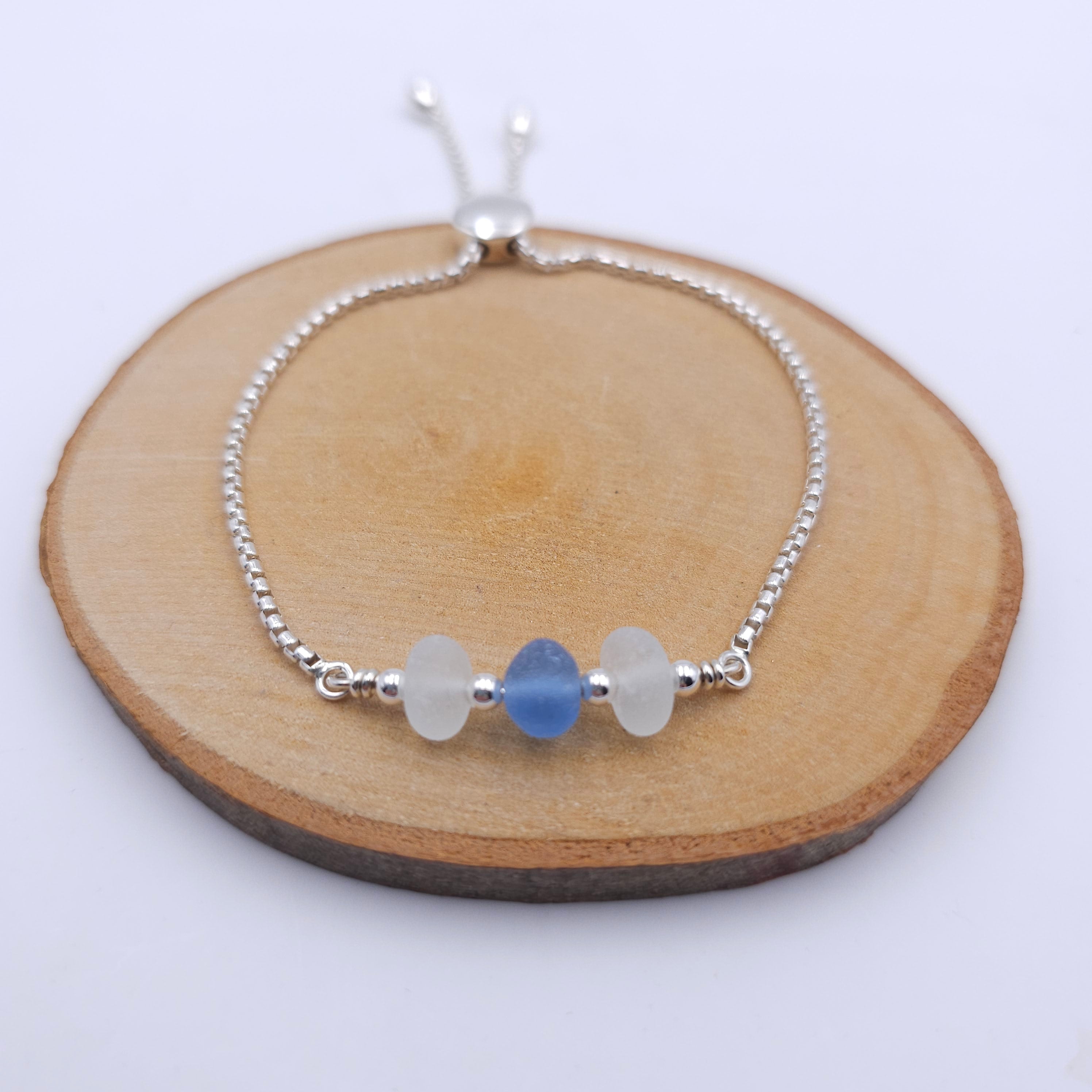 Silver chain bracelet with two pieces of white sea glass and one piece of light blue in the center, separated by small silver round beads. A silver bead at the bottom slides to adjust the size.