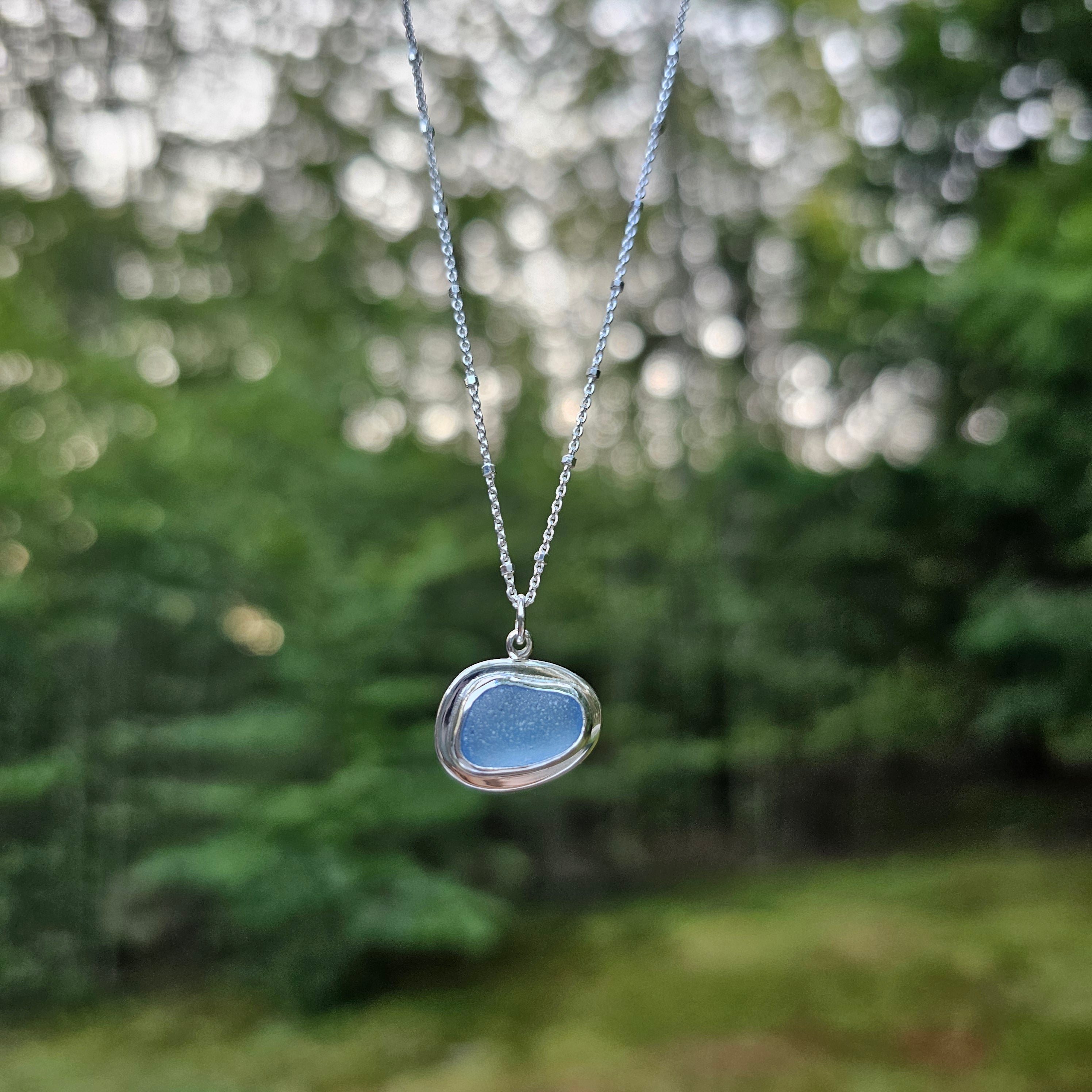 Light blue sea glass bezel set necklace with silver border. Sea glass is a free form oval ish shape hanging horizontally.